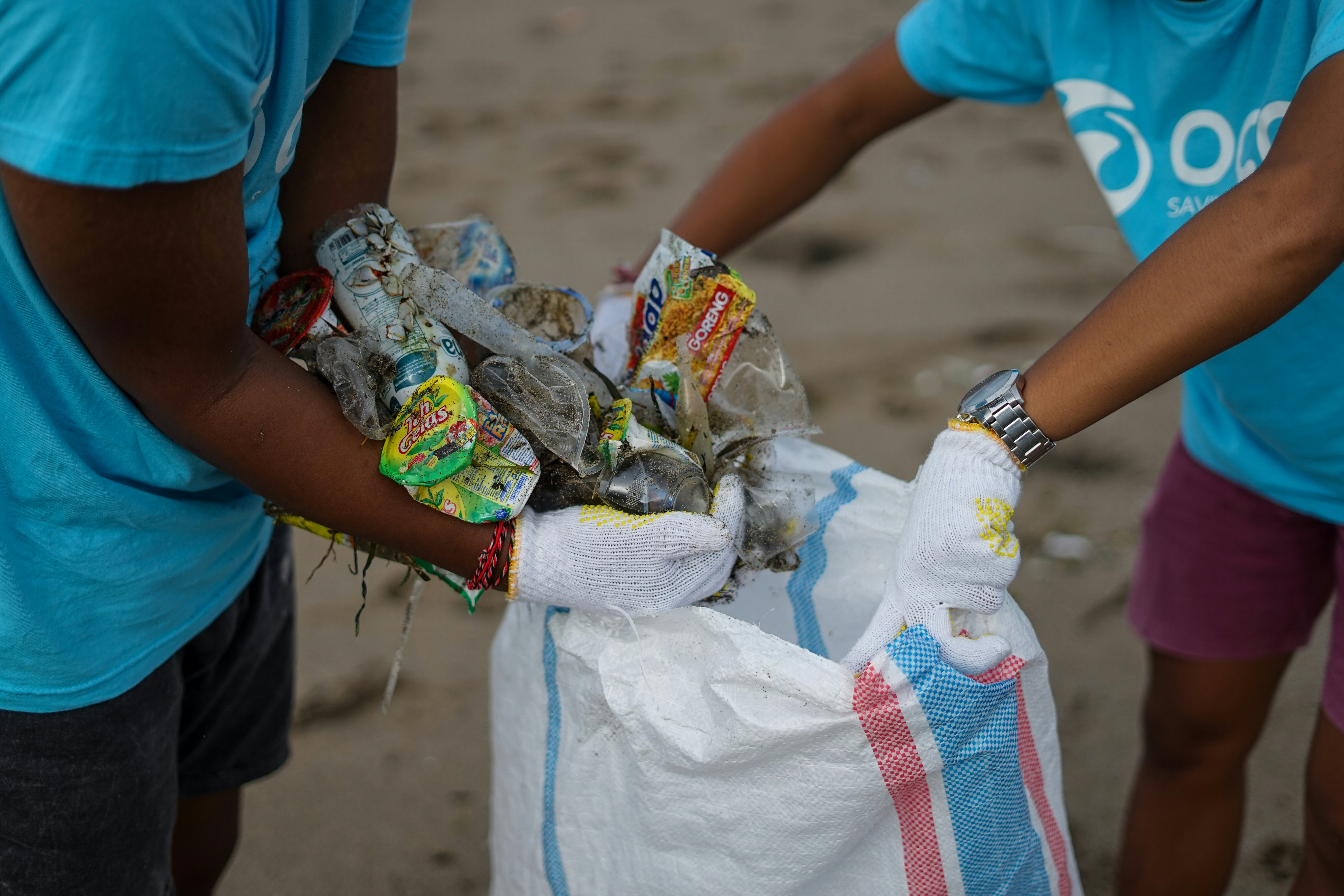 Two people working together to take garbage out of the beach and into a biodegradable bag